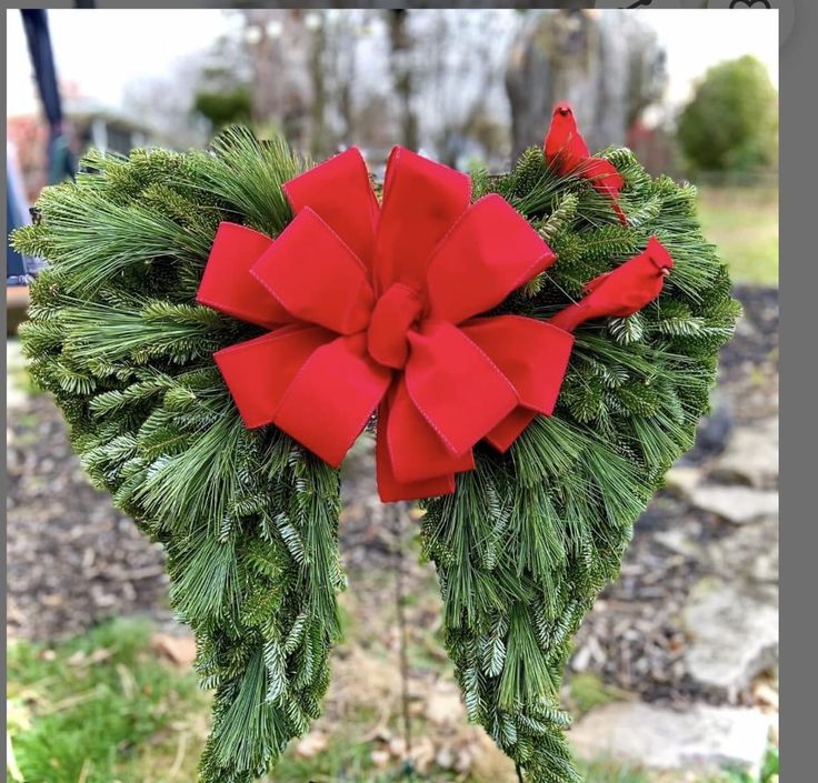 a red bow on top of a green wreath with pine needles in the shape of a heart