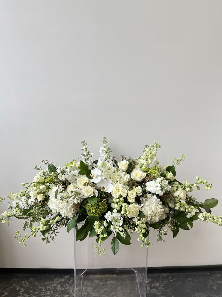 a clear vase filled with white flowers and greenery