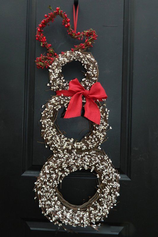 a wreath hanging on the front door with a red bow and two other wreaths attached to it