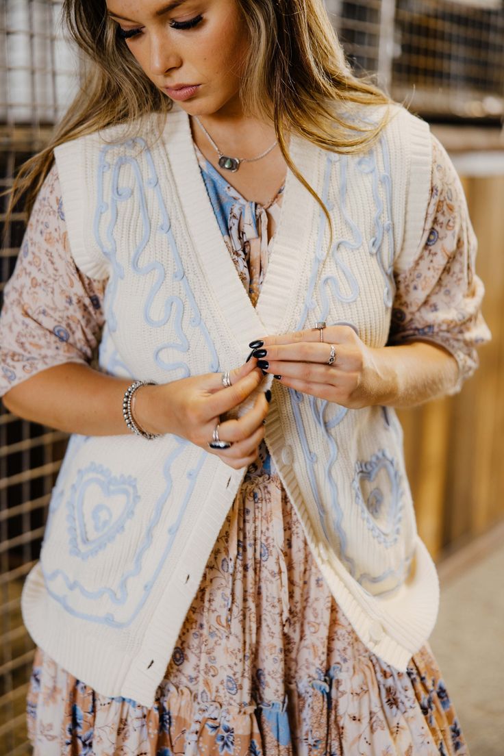 Introducing The Rachel Vest - a playful spring and summer layering piece with a blue embroidered detail. This collarless, button-up sweater vest top comes in a cream/blue color that will add a touch of quirkiness to any outfit. Haylee is wearing size small paired with The Jane Dress Trendy Blue Vest For Spring, Bohemian V-neck Vest For Spring, Fitted Sweater Vest For Spring Day Out, Cotton Vest For Day Out In Spring, Fitted Sweater Vest For Spring Layering, V-neck Sweater Vest For Spring Layering, V-neck Sweater Vest For Spring Day Out, Spring V-neck Sweater Vest For Day Out, Beige Vest For Day Out In Spring