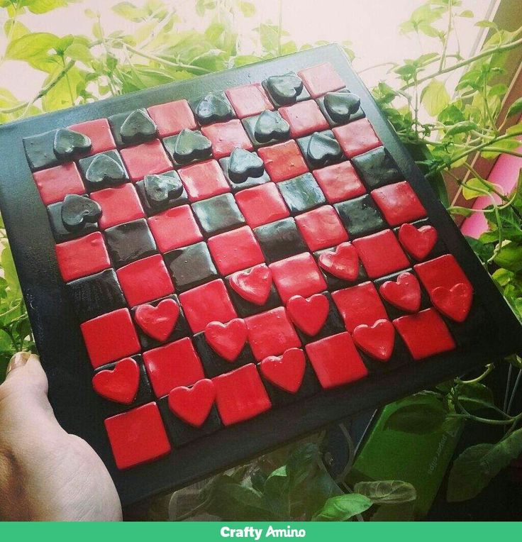 a person holding up a red and black tile with hearts on it in front of some plants