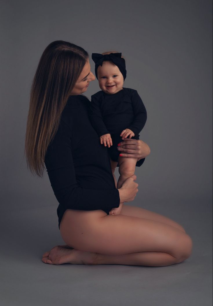 a woman holding a baby in her arms and smiling at the camera while sitting on the floor