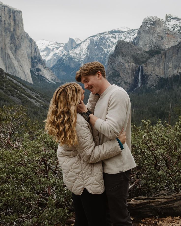 a man and woman standing next to each other in front of mountains with snow on them