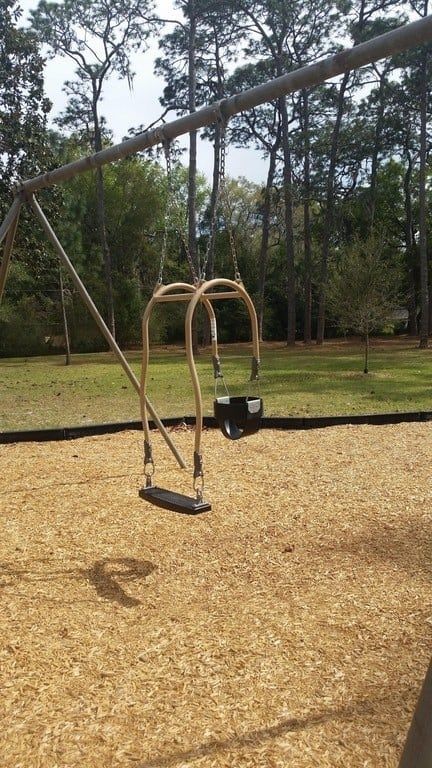 a swing set in the middle of a park with trees in the backgroud