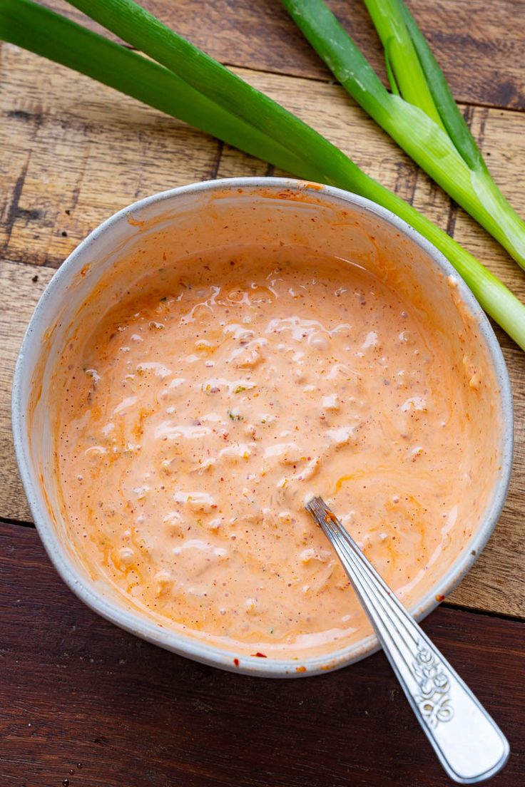 a bowl filled with sauce next to green onions on top of a wooden table,