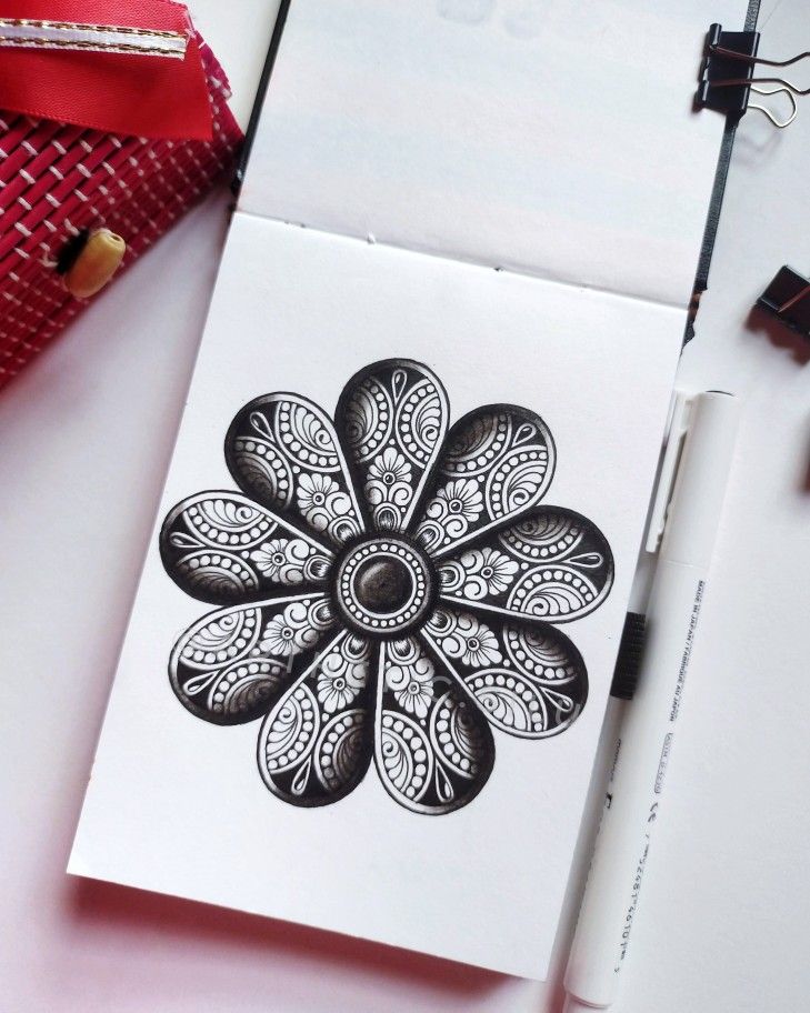 a white paper with a black and white flower design on it next to some pens