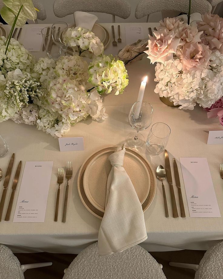 the table is set with silverware and white napkins, gold place settings and flowers