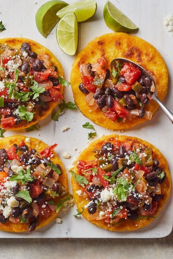 four tortillas topped with black beans, tomatoes and cilantro on a cutting board