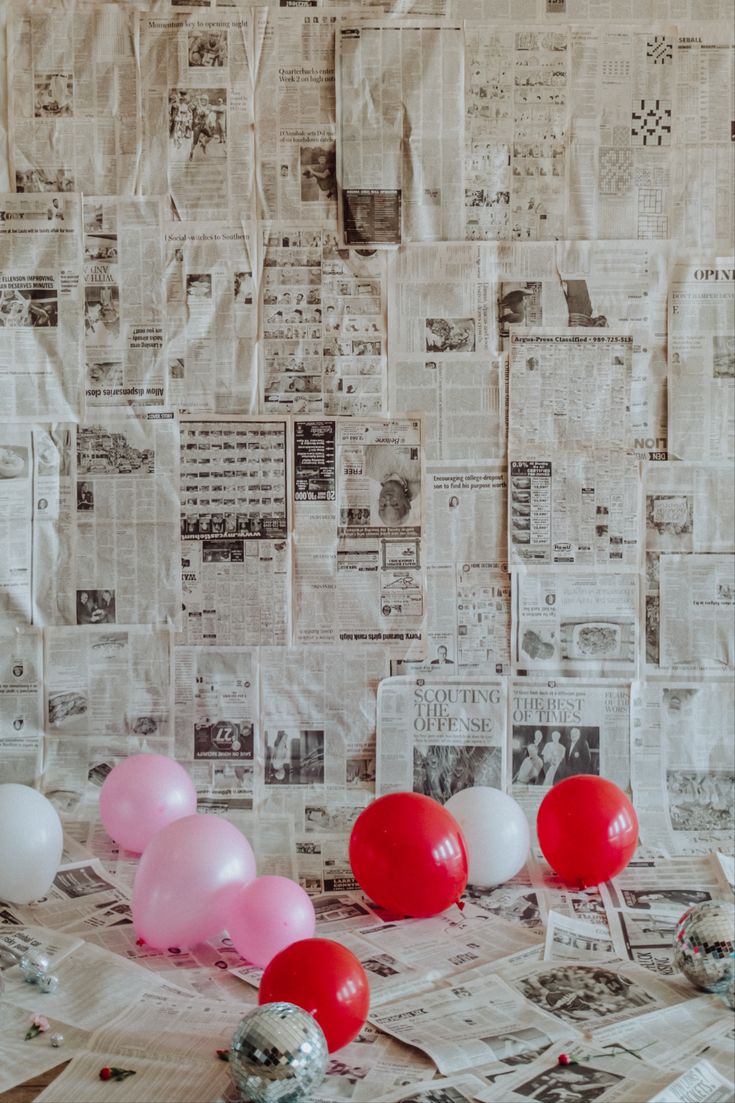 red and white balloons are on the table in front of newspaper wallpaper with pink and white balloons