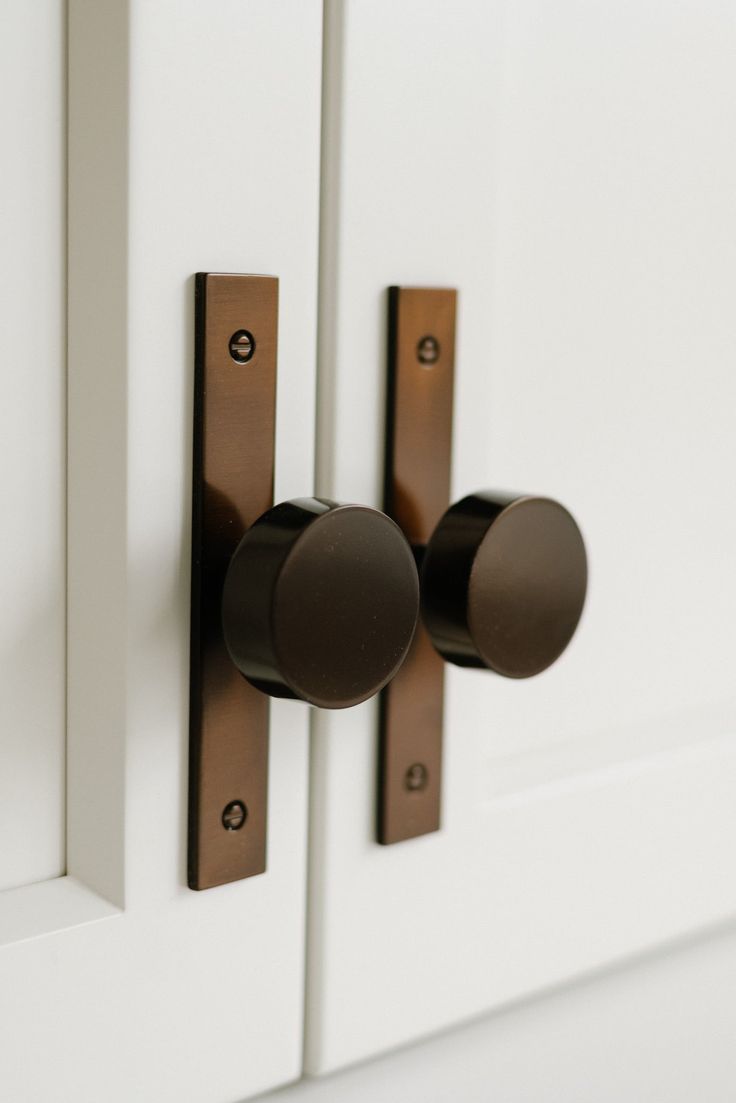 two knobs on the front of a white cabinet with brown handles and round knobs