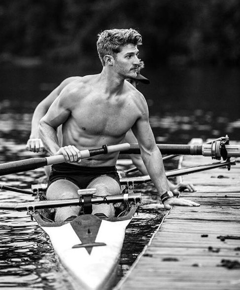 a shirtless man sitting on top of a boat in the water with two oars