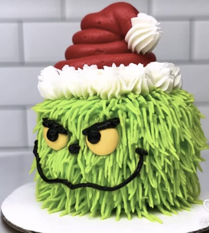 a green cake with white frosting and red icing on it's face