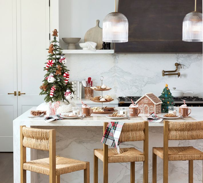 a kitchen with white marble counter tops and wooden chairs around a table covered in christmas decorations