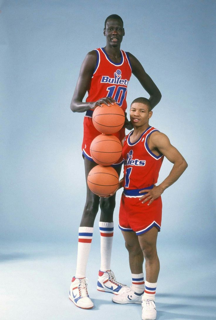 two basketball players pose for a photo with their balls in front of them, both wearing red and blue uniforms