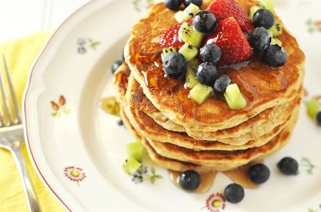 a stack of pancakes topped with fruit on top of a white plate next to a fork