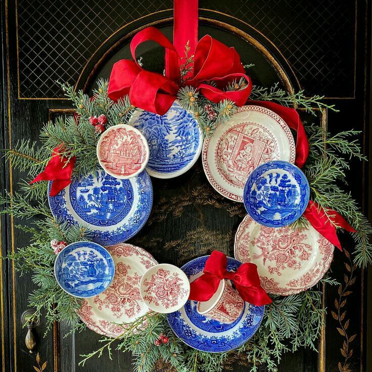 a christmas wreath with plates and red bows on the front door to give it a festive touch