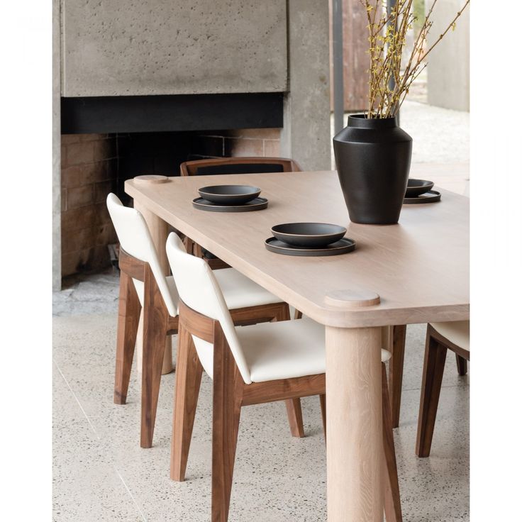 a wooden table with white chairs and a black vase