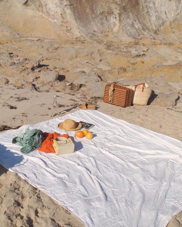 there is a white blanket on the beach with hats and other items sitting on it