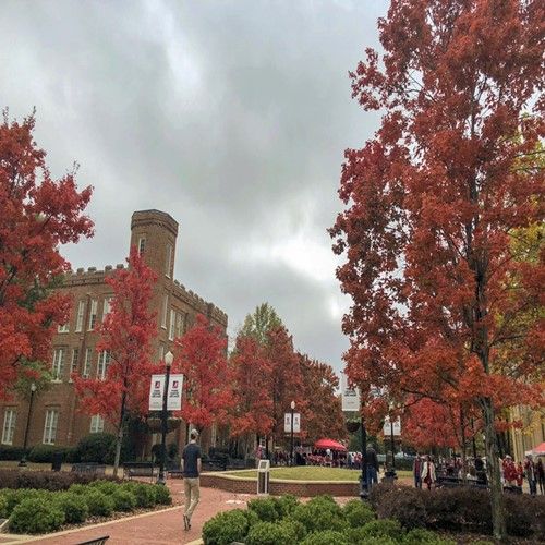 the trees are changing colors in front of an old brick building with people walking around