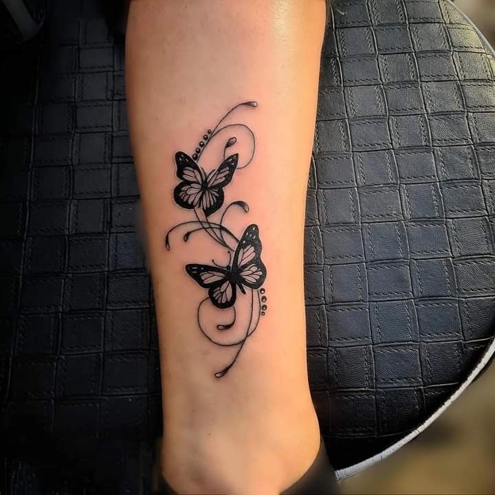 a black and white photo of a butterfly tattoo on the ankle, with swirls around it