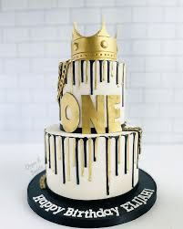 a three tiered birthday cake decorated with gold and black icing on a white table