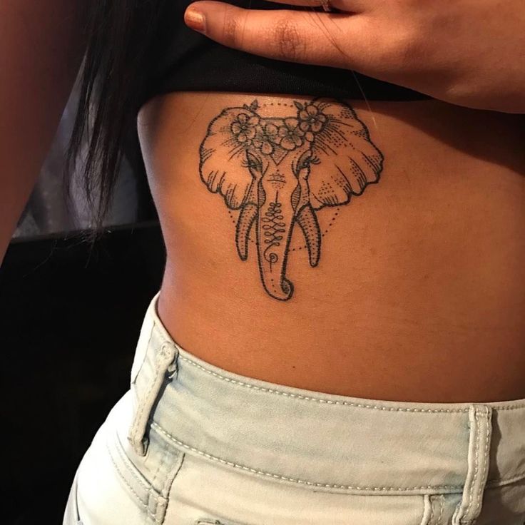 an elephant tattoo on the side of a woman's stomach, with flowers in its trunk