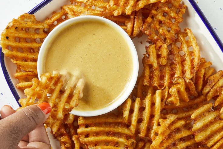 a person dipping something into a bowl of sauce on top of some cheesy fries