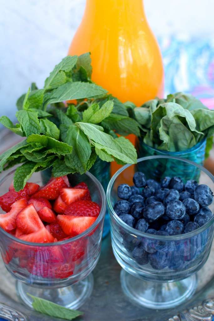 three bowls filled with berries and mint on top of a glass tray next to a bottle of orange juice