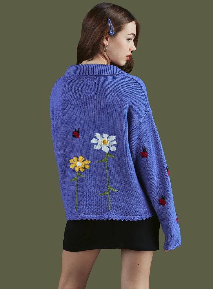 a woman wearing a blue sweater with flowers and ladybugs embroidered on the back