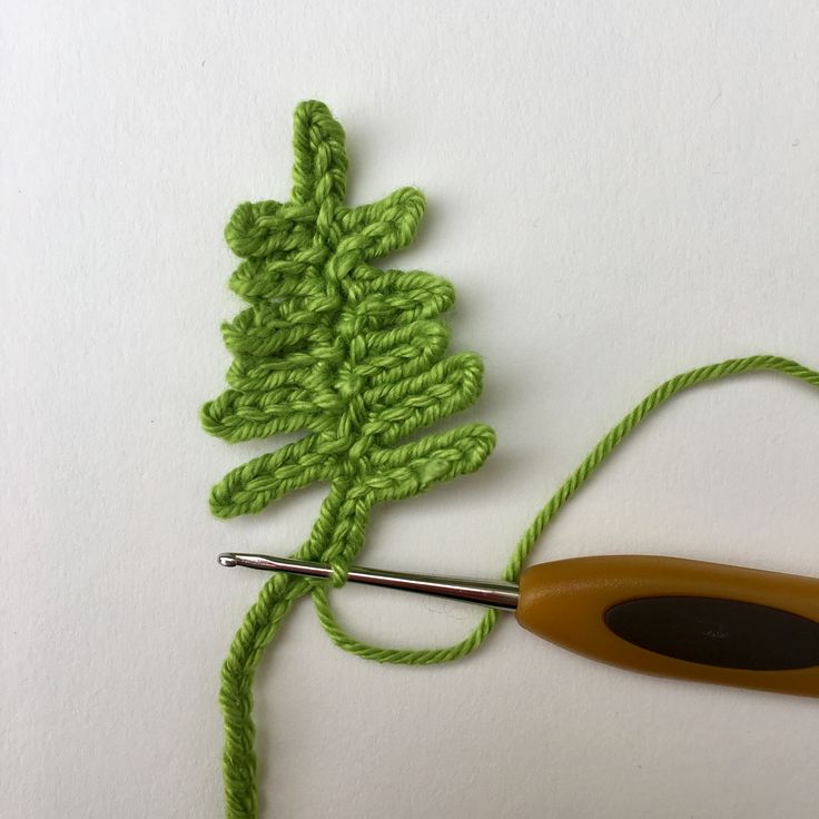 a crochet hook is hooked up to a green piece of yarn with a pair of scissors next to it