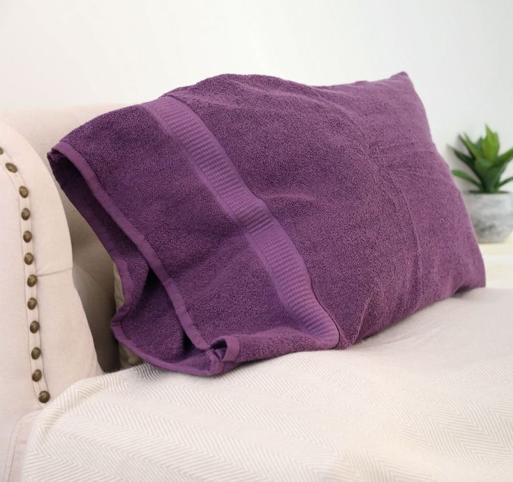 a purple pillow sitting on top of a white couch next to a potted plant