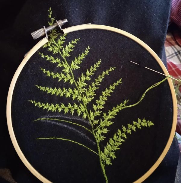 a close up of a embroidery on a black cloth with a green plant in the center