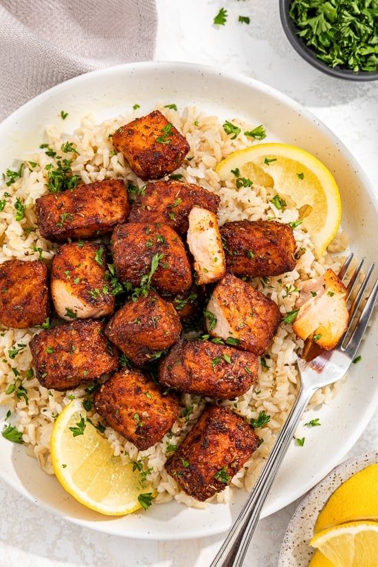 a white plate topped with chicken and rice next to lemon wedges