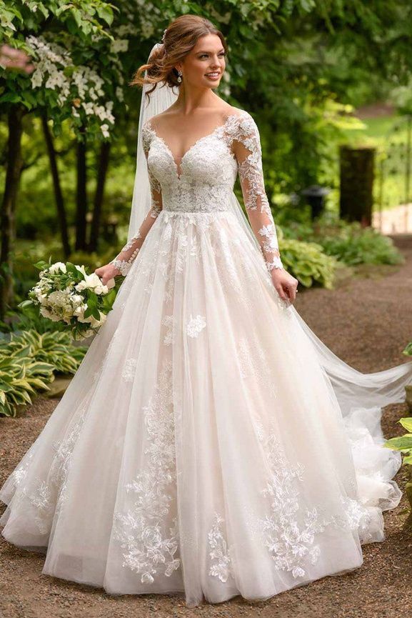 a woman in a wedding dress standing on a path with trees and flowers behind her