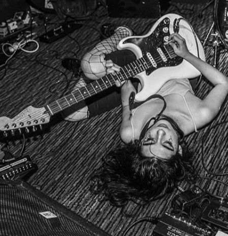 a woman laying on the floor with a guitar in front of her and other musical equipment around her