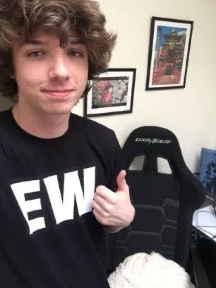 a young man giving the thumbs up sign in front of a desk with pictures on it