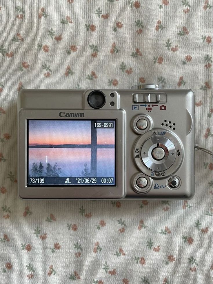 a camera sitting on top of a bed next to a flowered sheet with the sun setting