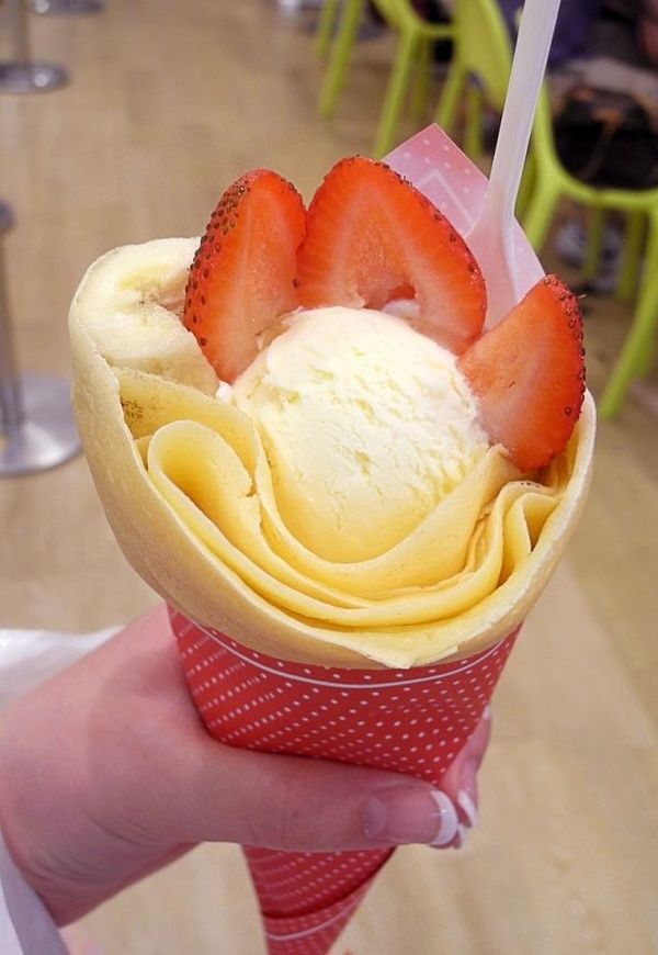 a person holding up an ice cream sundae with strawberries on top in a restaurant