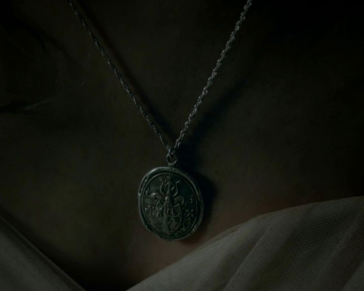 a woman wearing a necklace with a medallion on it's neck in the dark