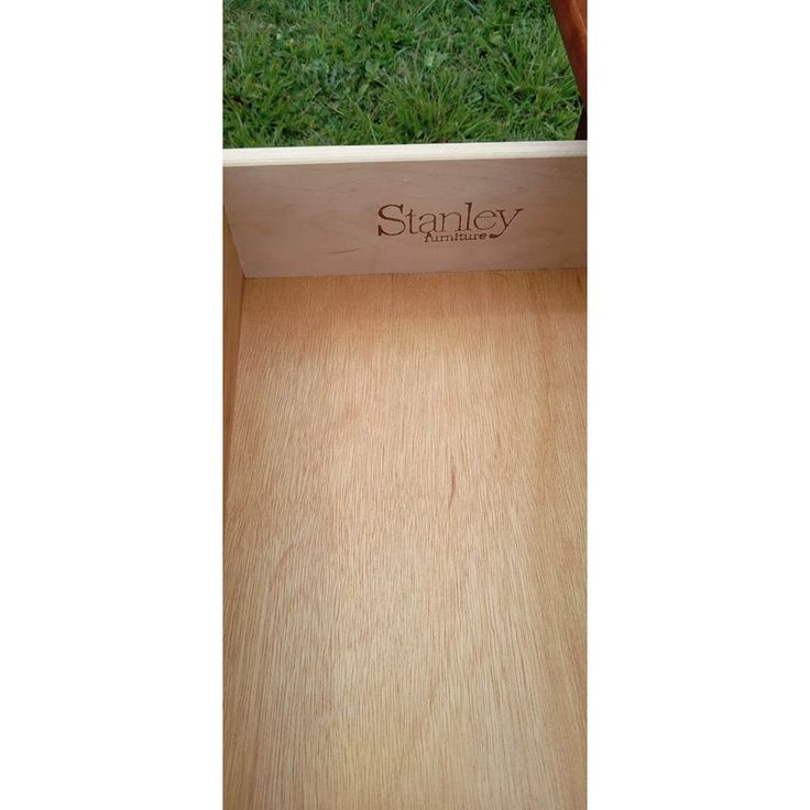 an empty wooden box sitting on top of a green grass covered field with the word stanley printed on it