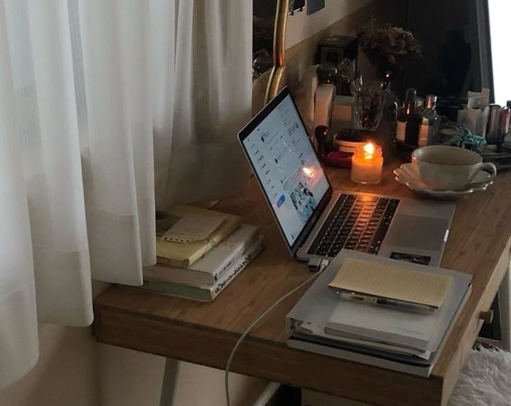 an open laptop computer sitting on top of a wooden desk next to a window with white curtains