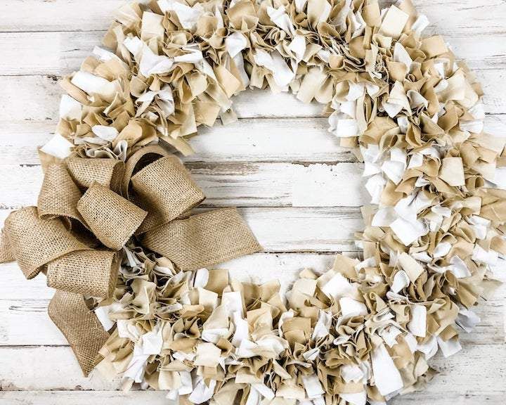 a wreath made out of burlock on top of a white wooden floor with a bow