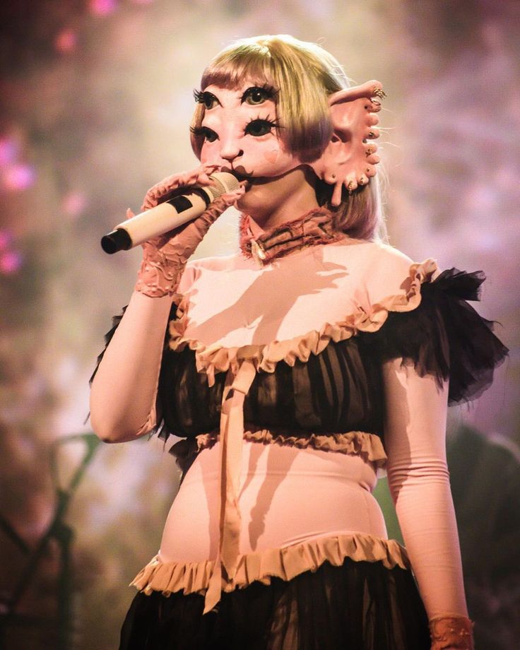 a woman in costume holding a microphone up to her mouth while standing on stage with lights behind her