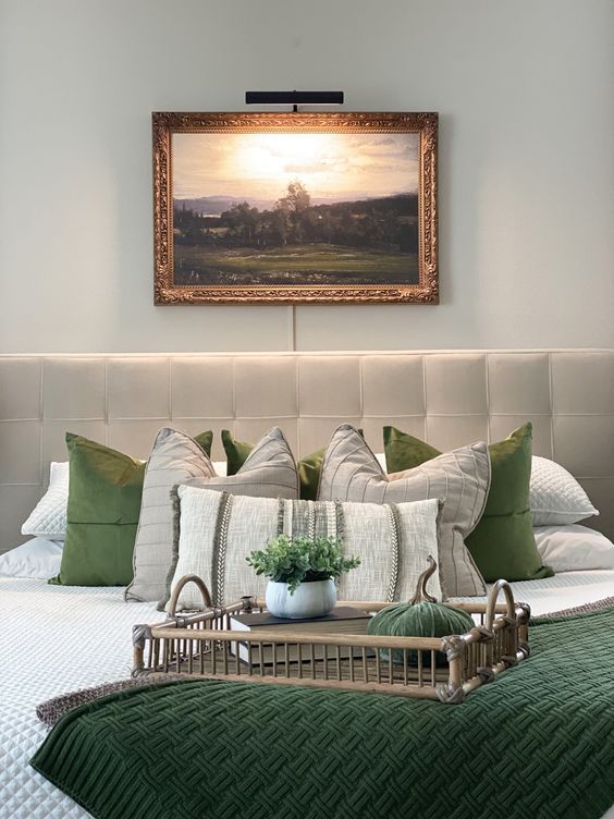 a bed with green pillows and white sheets in front of a painting on the wall