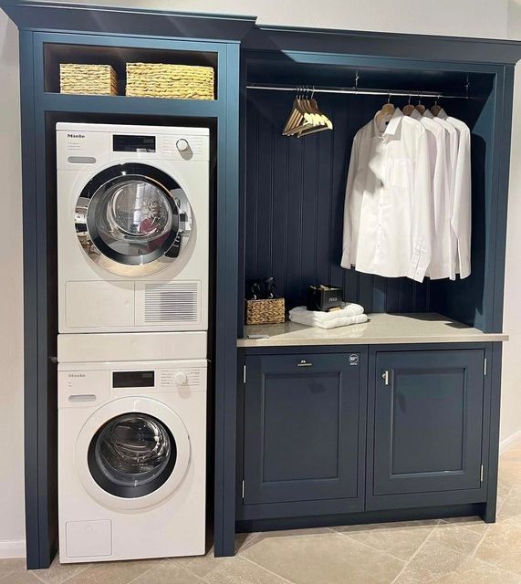 a washer and dryer in a room next to some cabinets with clothes hanging on them