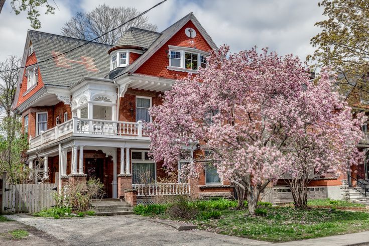 a red house with white trim and pink flowers on the tree in front of it