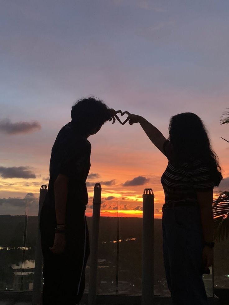 two people standing next to each other with their hands in the shape of a heart