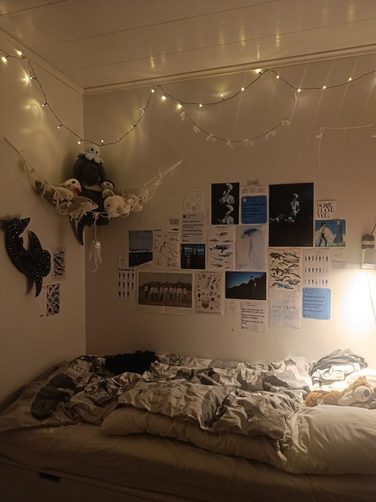 an unmade bed with lots of pictures on the wall and lights strung above it