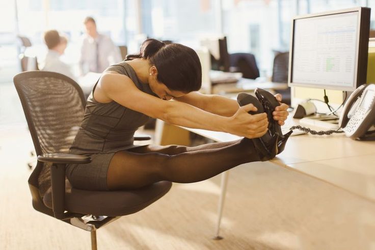 a woman sitting in an office chair with her foot on the computer desk and looking down