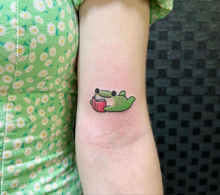 a woman with a small tattoo on her arm that has a crocodile reading a book